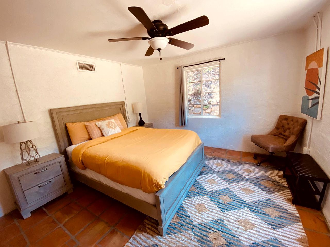 Une chambre à coucher comprenant un lit, une table de chevet, une chaise, un ventilateur de plafond, une fenêtre et un tapis.