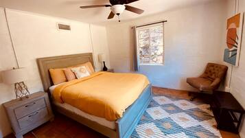 Une chambre à coucher comprenant un lit, une table de chevet, une chaise, un ventilateur de plafond, une fenêtre et un tapis.