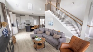 Ein modernes Wohnzimmer mit einem grauen Sofa, einem runden Couchtisch und einem braunen Ledersessel. Eine Treppe mit Holzwertung führt in eine obere Etage.