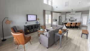 Ein modernes Wohnzimmer mit Sofa, Sessel und Couchtisch, eine Küche mit weißen Schränken und ein Essbereich mit Korbstühlen.