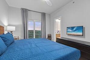 Ein Schlafzimmer mit einem großen Bett, einem an der Wand montierten Fernseher, einem Fenster mit Vorhängen und Blick ins Freie.