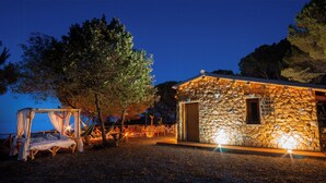A stone building with a wooden door, a hammock, and a bed under a tree. - Cottage with Aeolian Islands views near Cefalù (Cefalù)