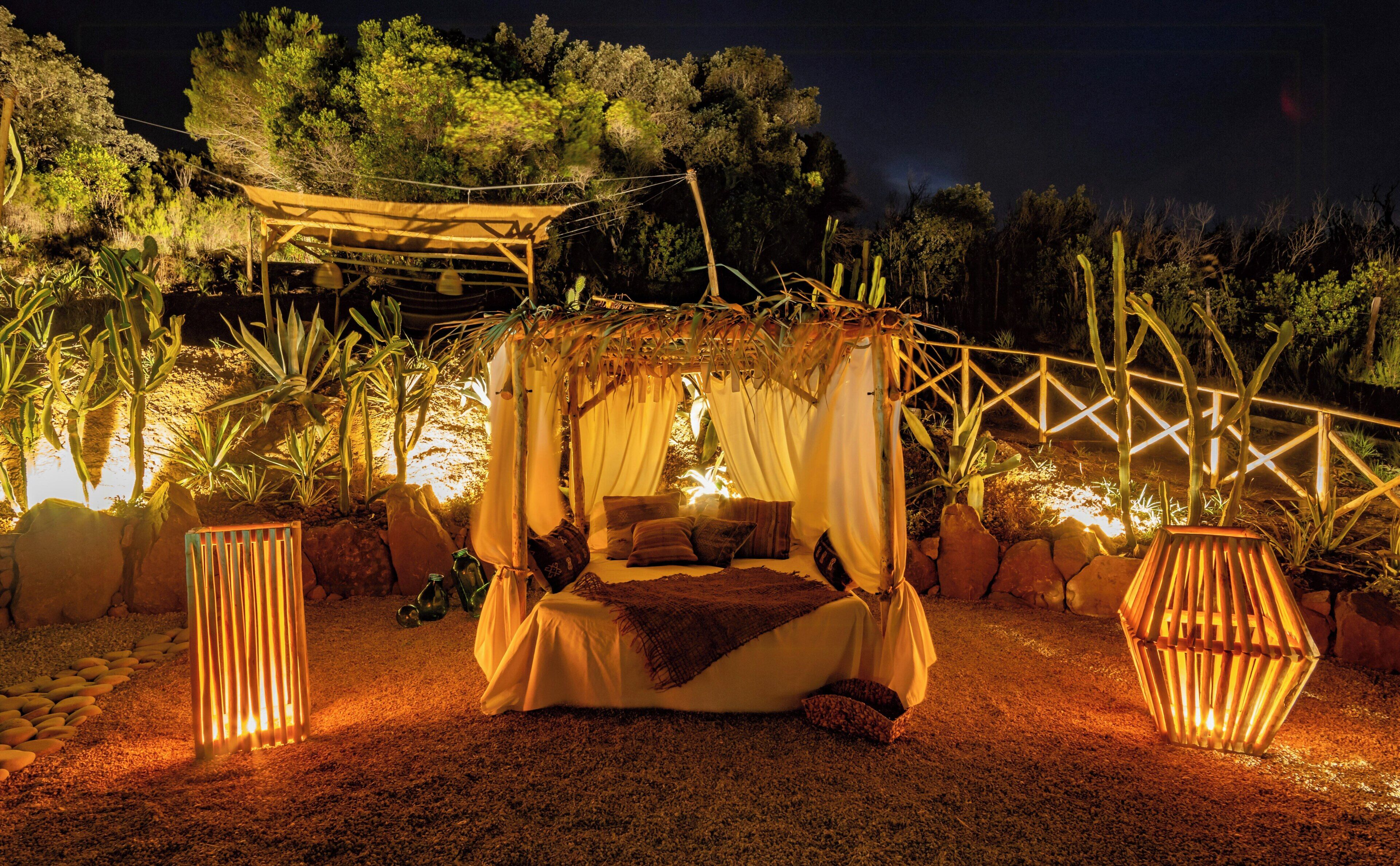 A cozy outdoor bed with a canopy, surrounded by plants and a wooden fence.