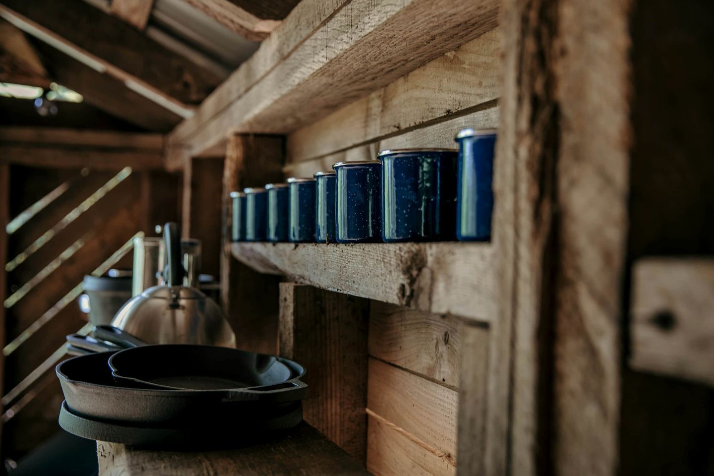 Un interior rústico de madera con una estantería que contiene varias latas azules, una sartén negra y un hervidor.