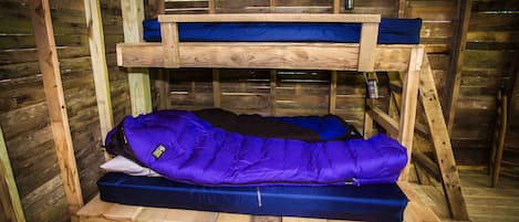 A bunk bed with a blue mattress and a purple sleeping bag.