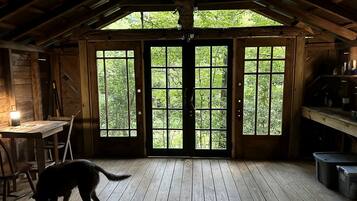 A rustic wooden interior with a large window, a dining table, and a cat.