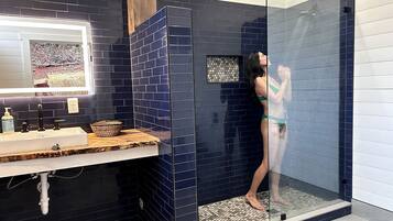 Ein Badezimmer mit Duschkabine, Waschbecken mit Spiegel und gefliestem Rücksprung.