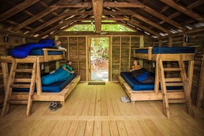 Una cabaña rústica de madera con literas, piso de madera y vista a la vegetación.