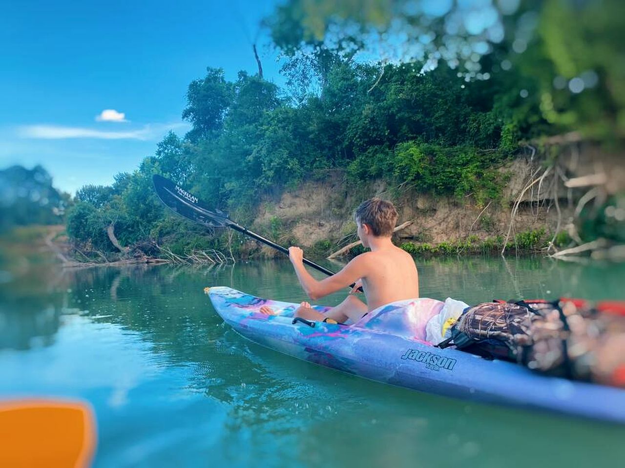 A person kayaking on a river surrounded by greenery.