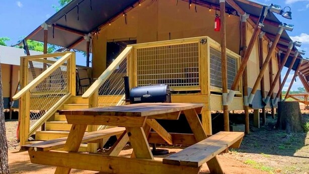 Une structure en bois comprenant une table de pique-nique et un barbecue, une zone délimitée par une clôture, et un bâtiment portant le numéro 49.
