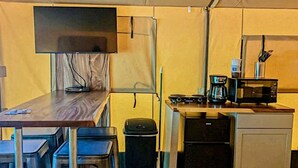 Une cuisine compacte équipée d’un four à micro-ondes, d’une machine à café et d’un petit réfrigérateur. On y trouve une table avec des chaises et un téléviseur fixé au mur.