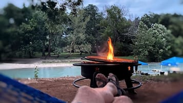A person relaxing by a campfire with a view of a lake and trees.