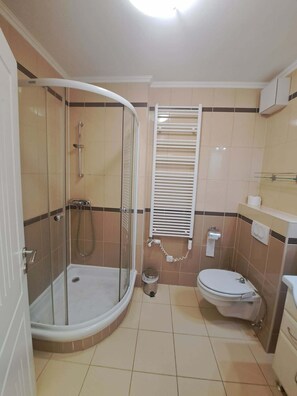 A bathroom with a glass-enclosed shower, a toilet, and a sink. - LSC Apartmenthotel (Siófok)