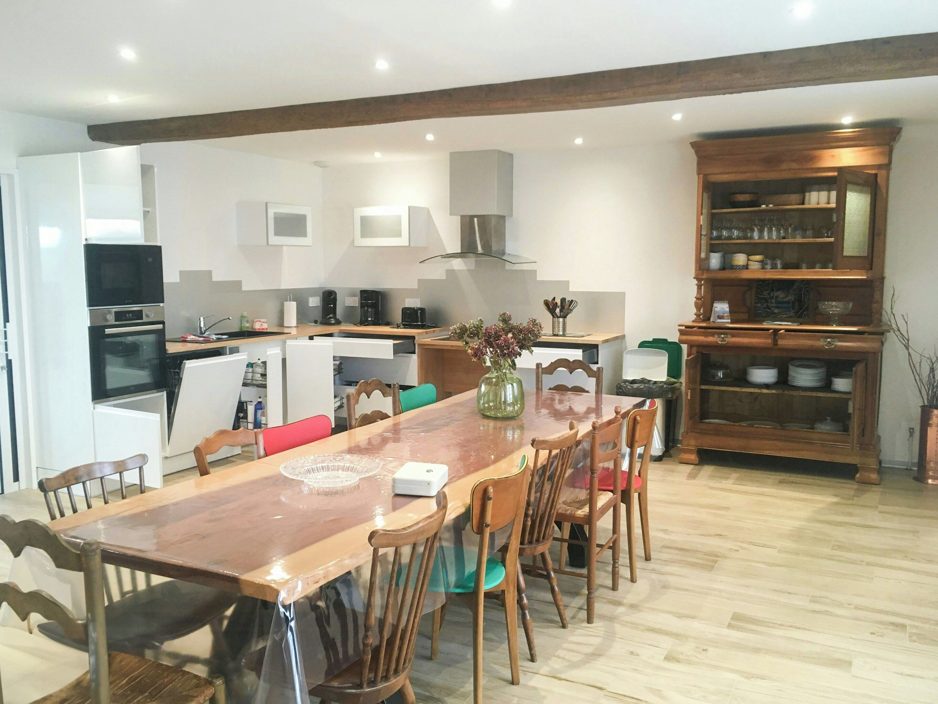A modern kitchen with built-in appliances, a dining area with wooden chairs, and a wooden cabinet with dishes.
