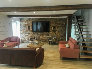 Ein Wohnzimmer mit Steinkamin, Flachbildfernseher, Treppe und zwei Sofas.