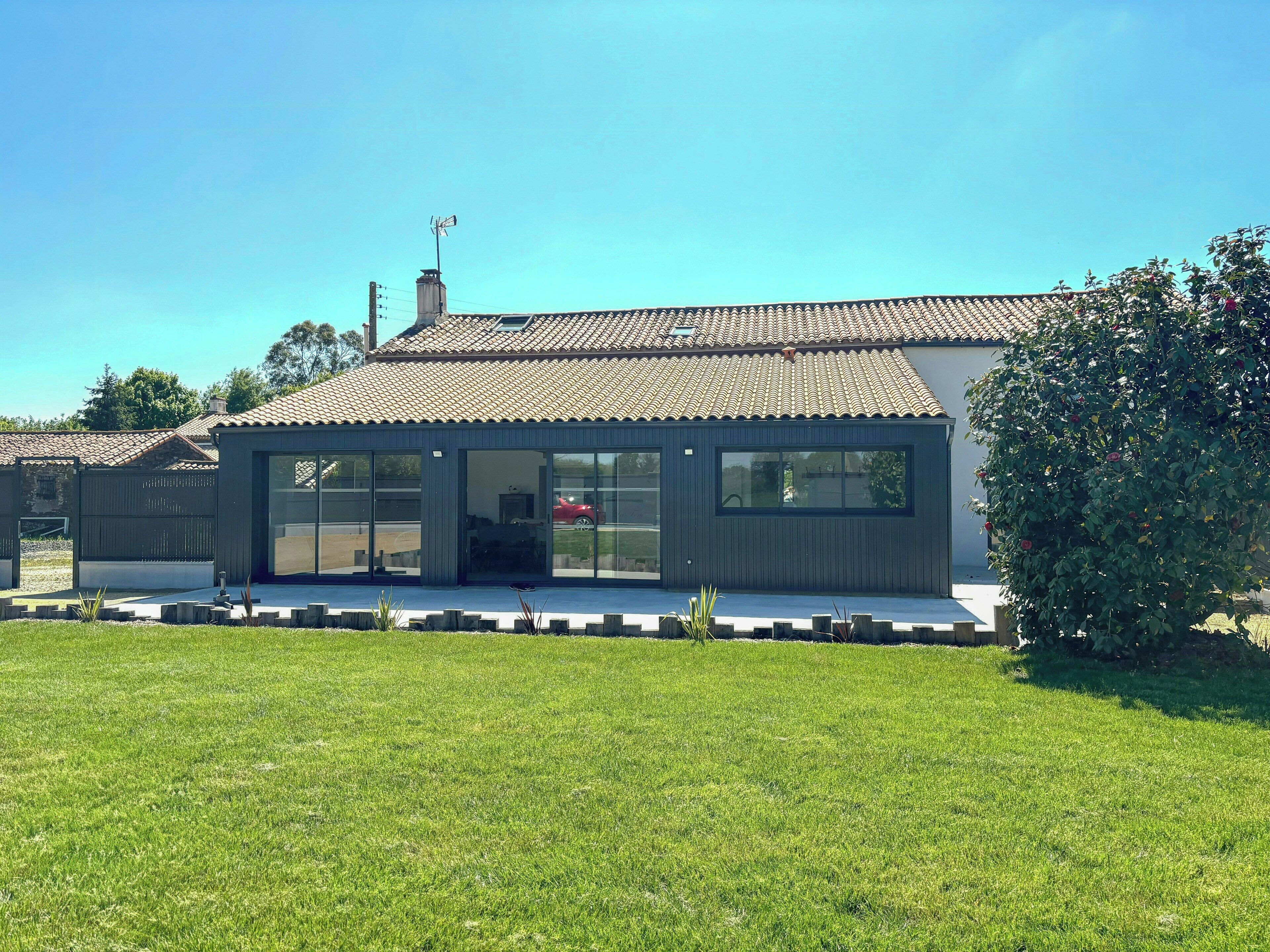 Une maison moderne avec un toit recouvert de tuiles, de grandes fenêtres et une pelouse bien entretenue.