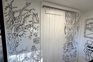 Um corredor com porta branca, decorado com desenhos em preto de árvores, corujas, cogumelos e um gato.
