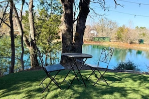 A picnic table and chairs by a lake with trees in the background. - Whimsical Lakefront Tiny Home with Hand-Drawn Doodle Design Near Bastrop, Texas (Bastrop)
