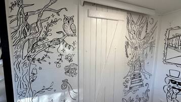 A hallway with a white door, decorated with black line drawings of trees, owls, mushrooms, and a cat.