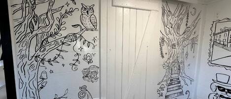 A hallway with a white door, decorated with black line drawings of trees, owls, mushrooms, and a cat.