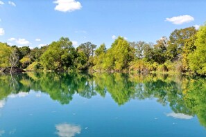 A calm lake with clear reflections of trees and sky. - Whimsical Lakefront Tiny Home with Hand-Drawn Doodle Design Near Bastrop, Texas (Bastrop)