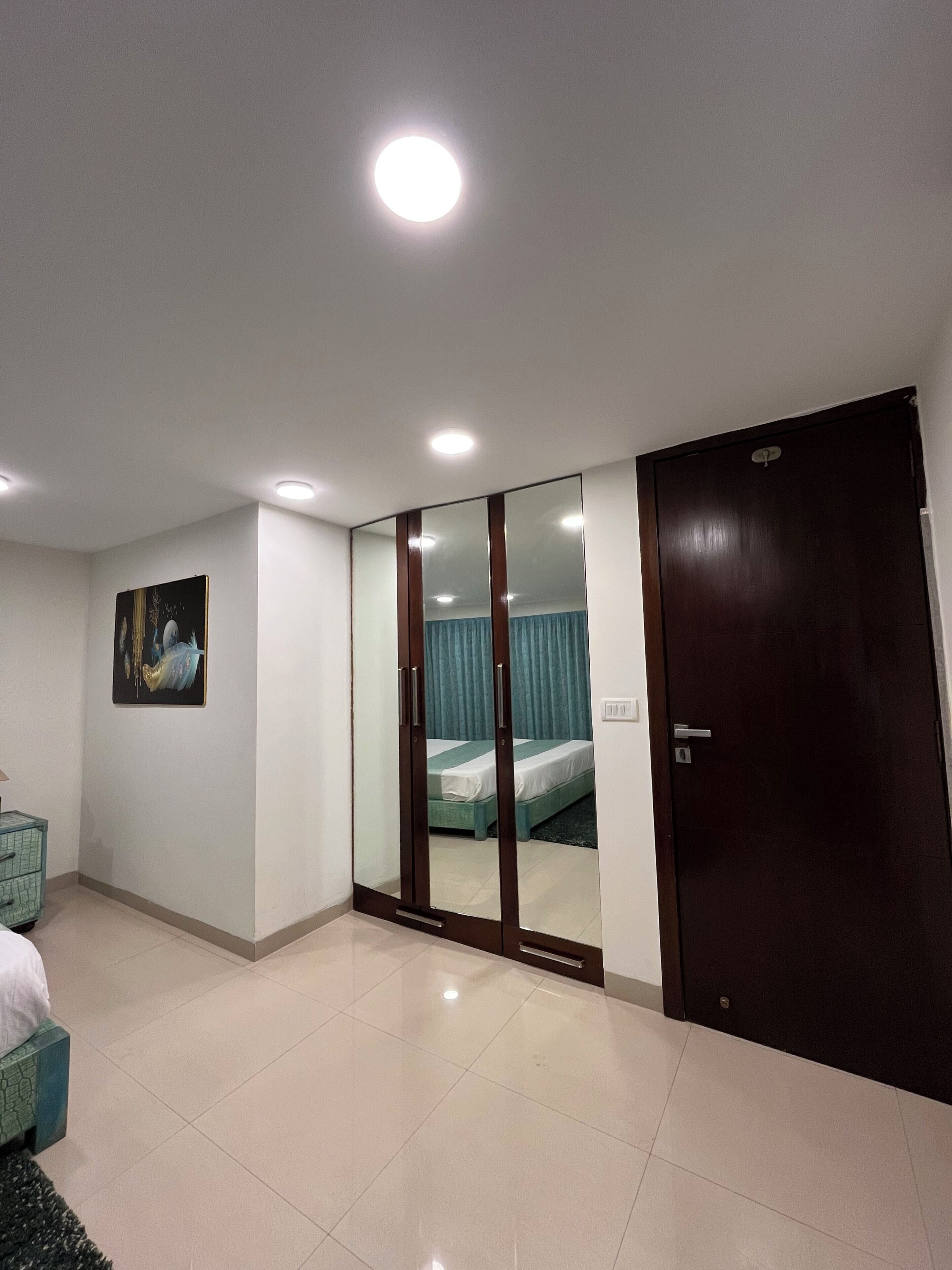 A hotel room with a bed, a wardrobe, a mirror, and a painting on the wall.