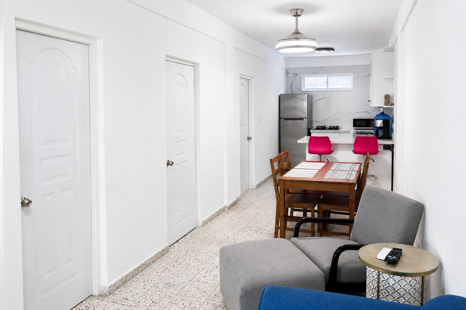 A narrow hallway leading to a kitchen with a dining area, a small table with a chair, and a sofa.