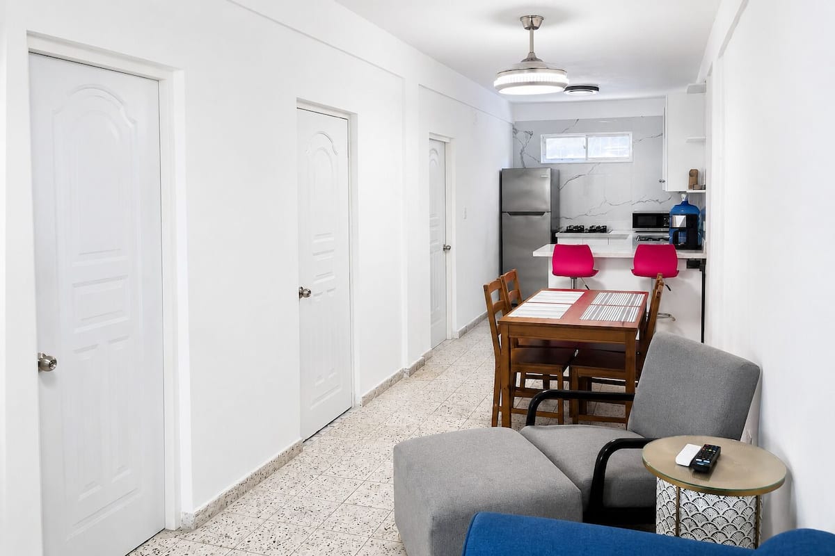 A narrow hallway leading to a kitchen with a dining area, a small table with a chair, and a sofa.