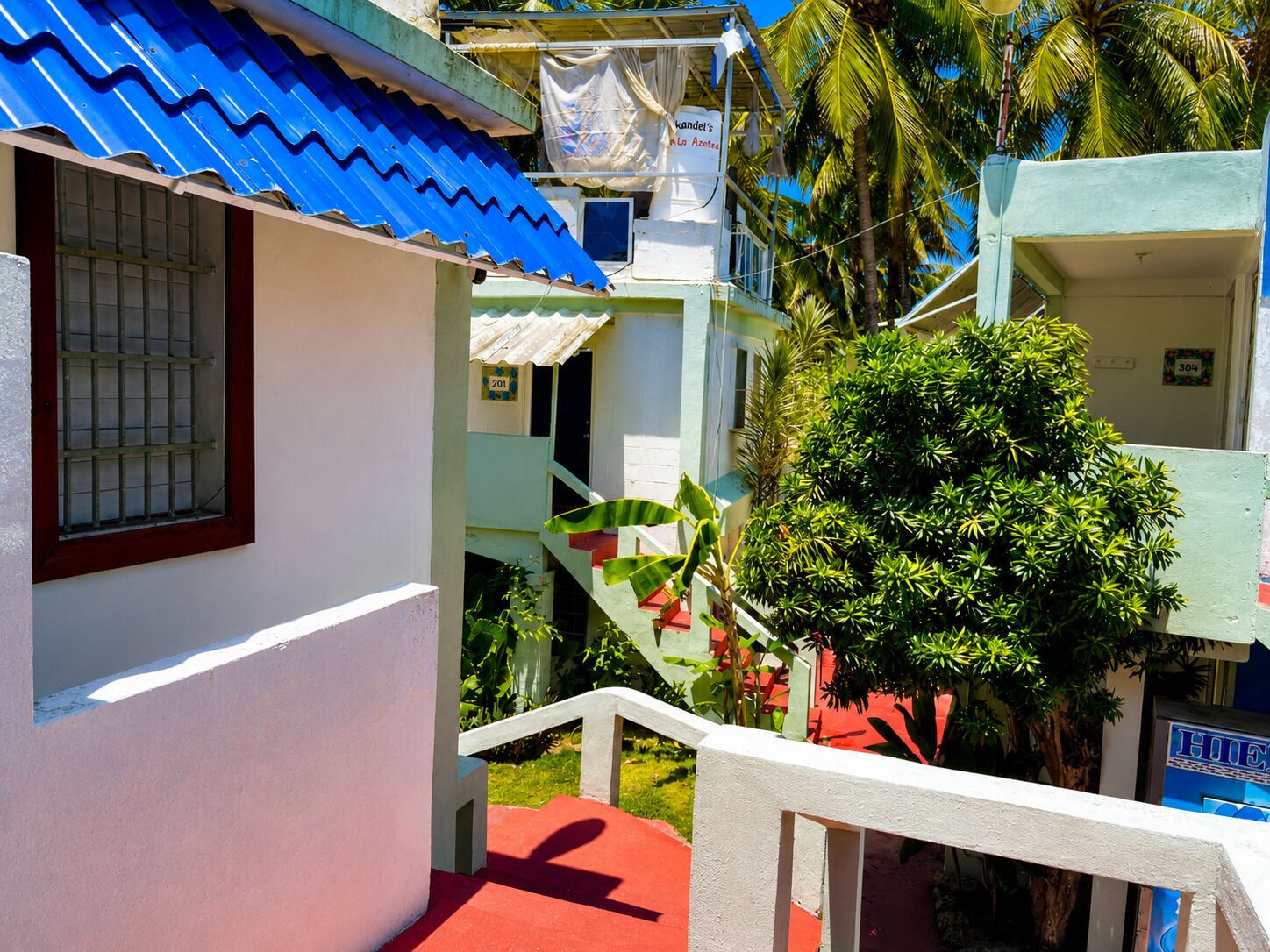 A narrow pathway leading to a building with a blue roof, a sign reading 'Kandel's in La Azotea,' and a number '201' on a window.