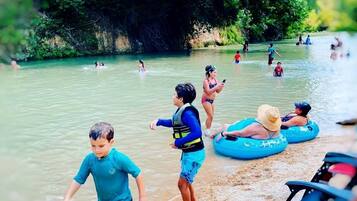 A river with people swimming and floating, surrounded by greenery.