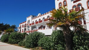 A white building with red accents, multiple balconies, and a palm tree in the foreground. - Seaside Apartment for 6 in Loire (La Tranche-sur-Mer)