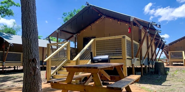 Una cabaña de madera con un porche cubierto, una mesa de picnic y una parrilla.