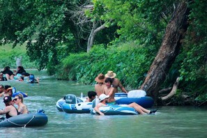 Menschen auf Luftmatratzen in einem von Grünpflanzen umflossenen Fluss.