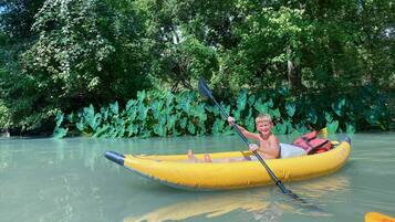 A person in a yellow inflatable raft on a calm river surrounded by dense green foliage.