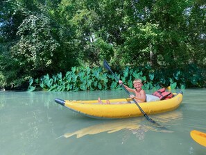 Uma pessoa em um bote inflável amarelo em um rio calmo, cercada por vegetação verde densa.