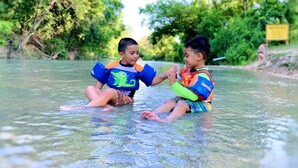 Due bambini che giocano in acqua bassa, circondati dal verde.