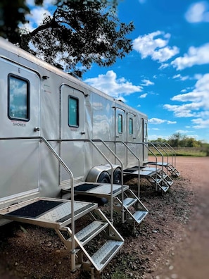A row of mobile homes with external shower facilities, metal stairs, and a dirt ground. - Dreamy Oasis on the San Marcos River: Luxurious Safari Tent Perfect for Glamping near Kingsbury, Texas (Kingsbury)