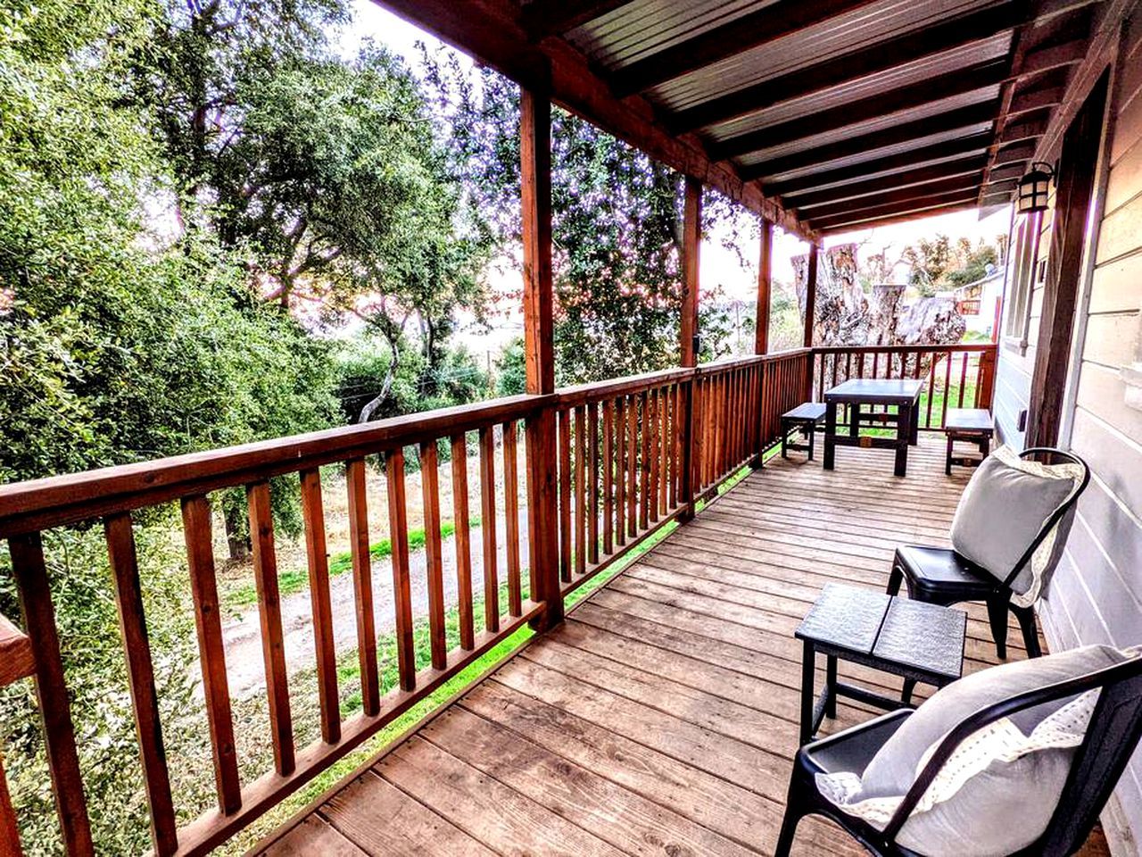 Une terrasse en bois avec une rambarde, des meubles d’extérieur et une vue sur les arbres et la verdure.