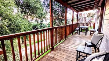 Une terrasse en bois avec une rambarde, des meubles d’extérieur et une vue sur les arbres et la verdure.