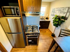 A compact kitchen with a built-in microwave, stove, and oven, wooden cabinets, and a potted plant.