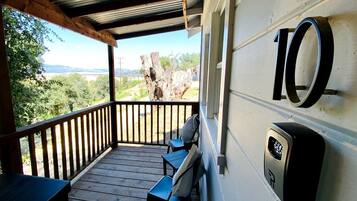 A covered outdoor area with a wooden deck, two chairs, a table, and a view of the landscape.