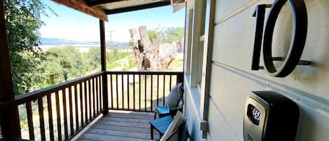 A covered outdoor area with a wooden deck, two chairs, a table, and a view of the landscape.