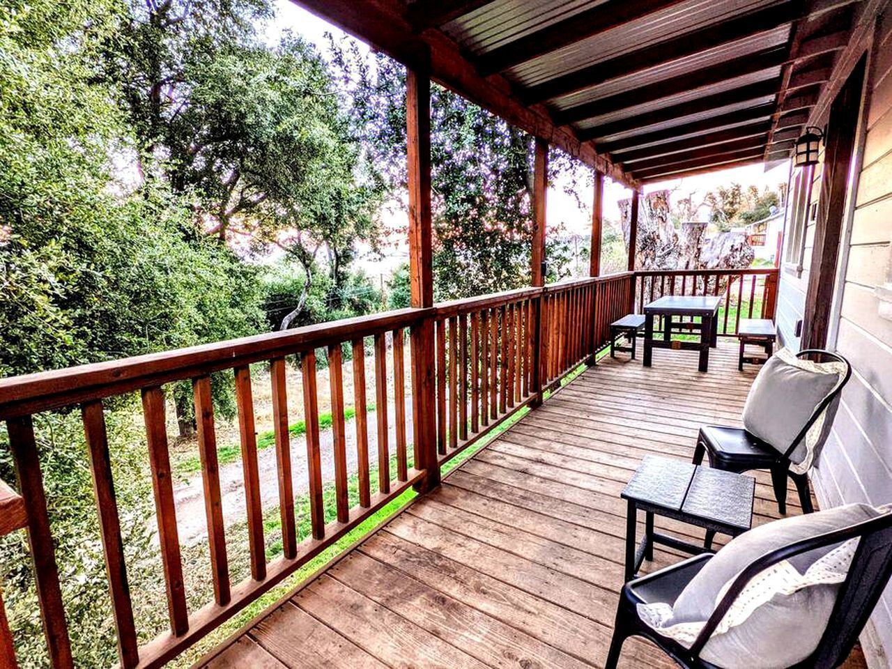 Une terrasse en bois avec une rambarde, des meubles d’extérieur et une vue sur les arbres et la verdure.
