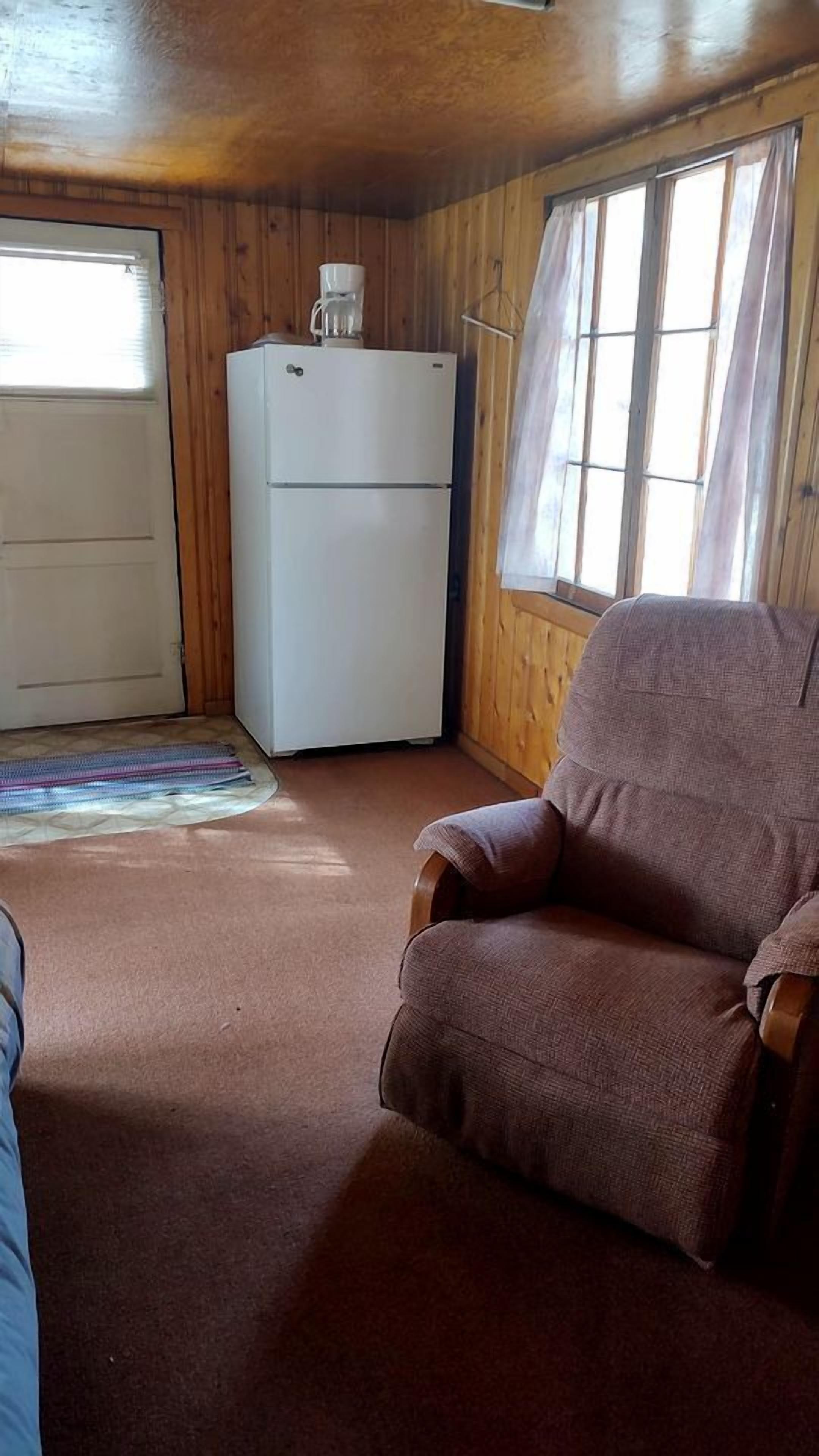 A wooden cabin interior with a refrigerator, a chair, and a door.