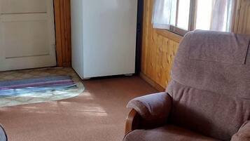 A wooden cabin interior with a refrigerator, a chair, and a door.