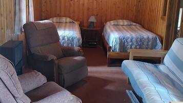 A room with two beds, a sofa, a chair, a lamp, and a framed picture on the wall.