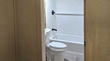 A bathroom with a toilet, bathtub, and white tiled walls.