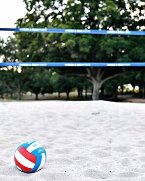 A volleyball on a sandy surface with trees and a blue banner in the background.