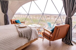 A cozy interior with a bed, a chair, a small table, and a view through a large window.