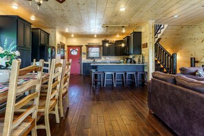 A cabin interior with a wooden floor, a dining area with chairs, a kitchen with dark cabinets, a bar area, and a staircase. - Outstanding Cabin with Game Room, Jacuzzi and Cinema Room in Tennessee (Sevierville)